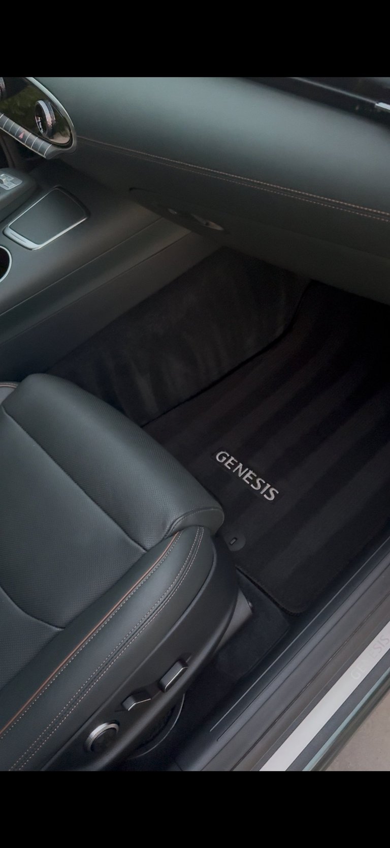 Interior view of a Genesis car showing the dashboard, steering wheel, and floor mats with Genesis branding