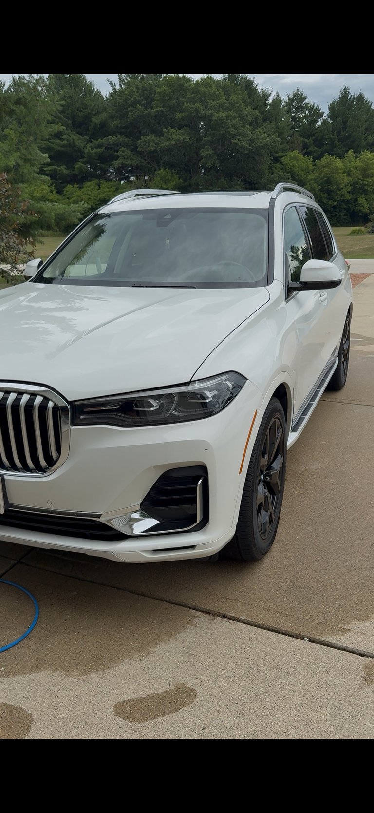 White BMW X7 SUV parked on concrete driveway with trees in background