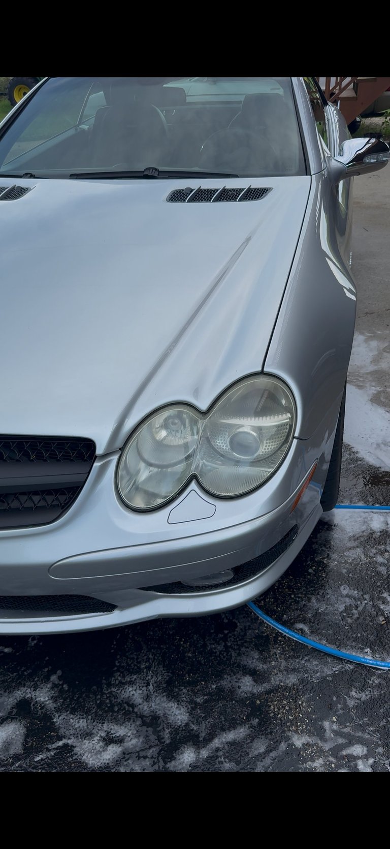 Front view of a silver Mercedes-Benz sedan parked in a driveway with dual round headlights visible