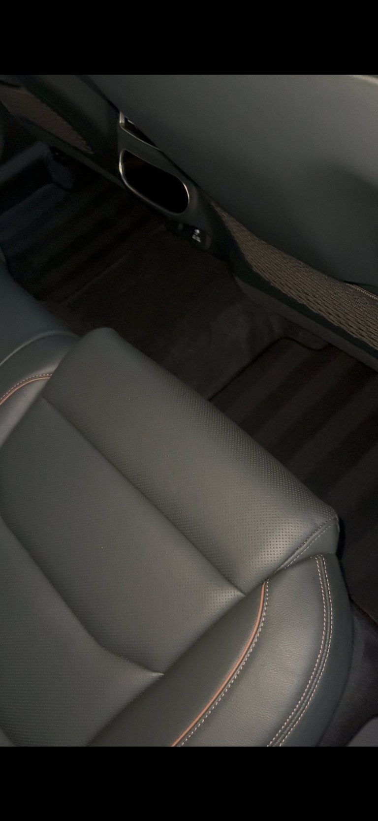 Interior car seat detail showing gray leather upholstery with orange stitching and black floor mats
