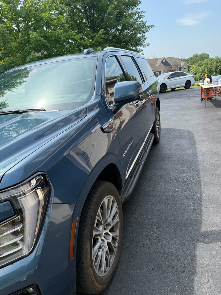 Dark blue GMC pickup truck parked in a paved lot with trees and houses visible in the background
