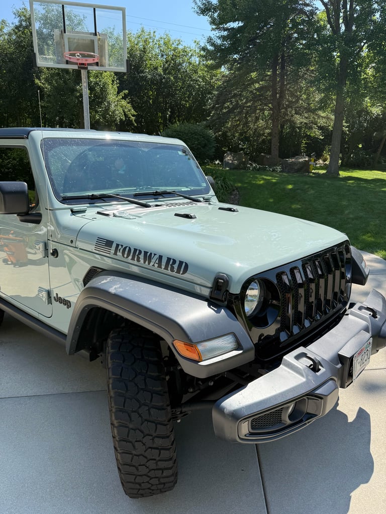White Jeep Wrangler parked in driveway with basketball hoop in background and trees